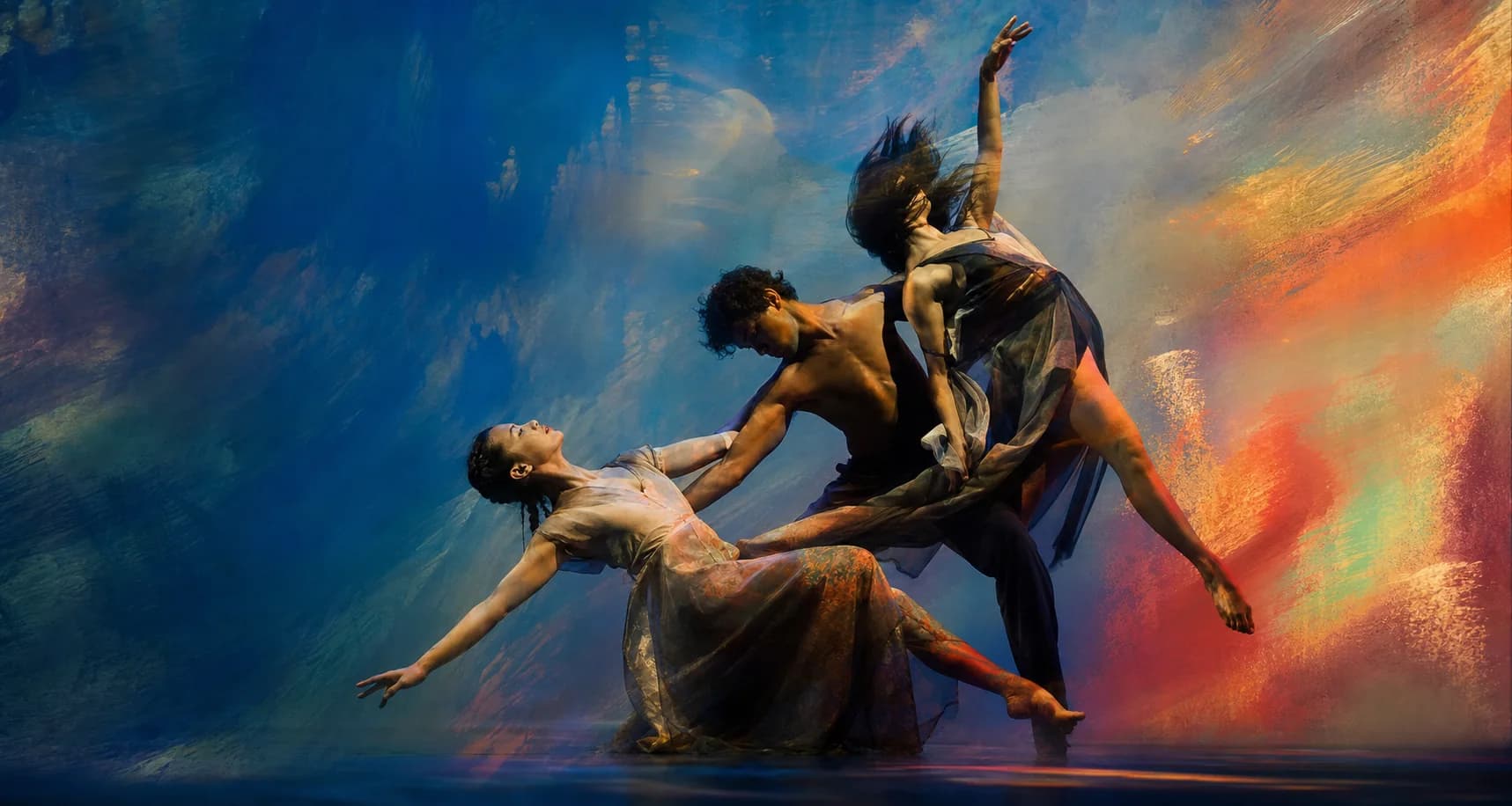 Three contemporary dancers forming an interlocking sculptural pose against cobalt and vermilion projections