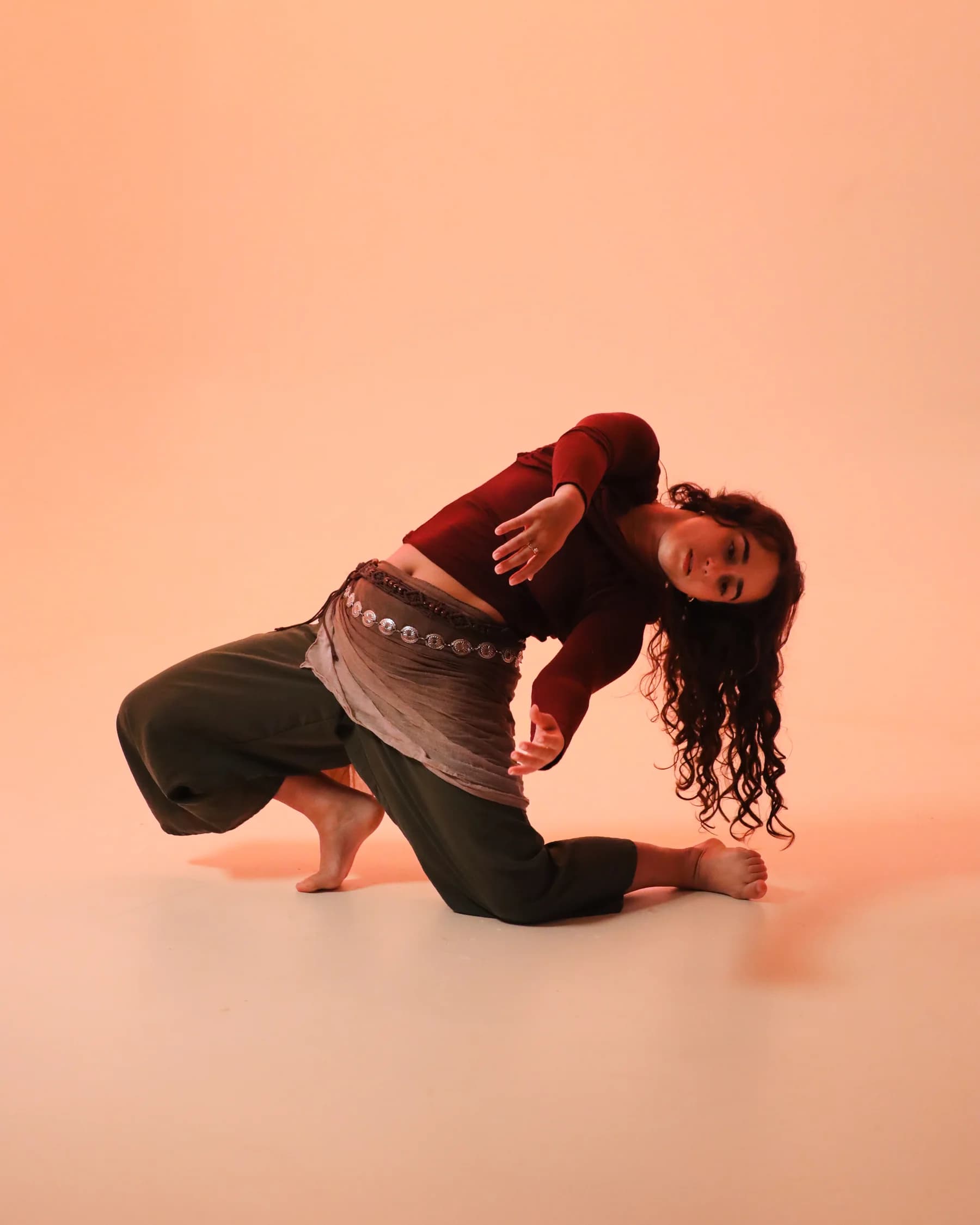 A dancer kneeling and arching sideways against a peach studio backdrop